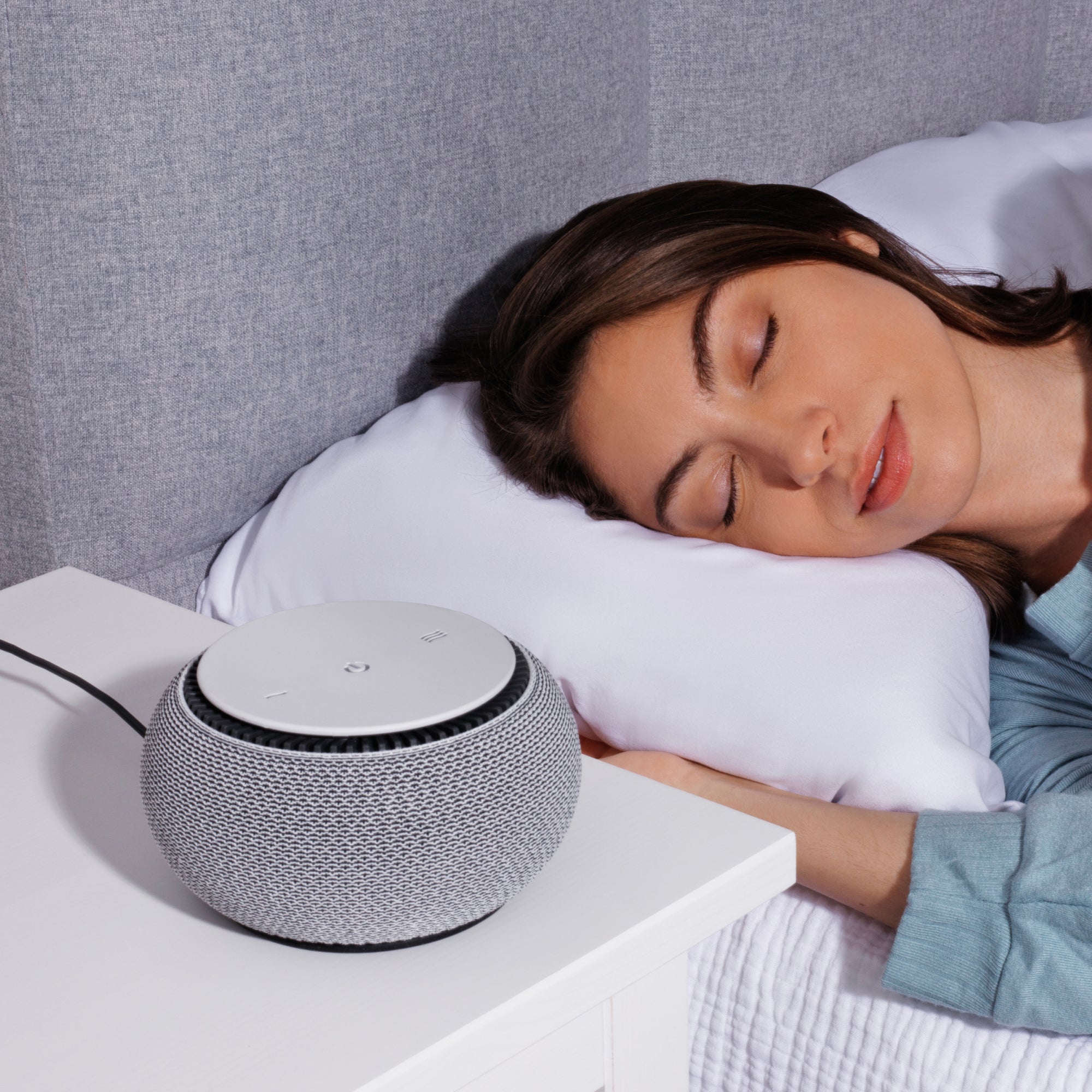Woman sleeping beside a gray smart speaker on a nightstand.