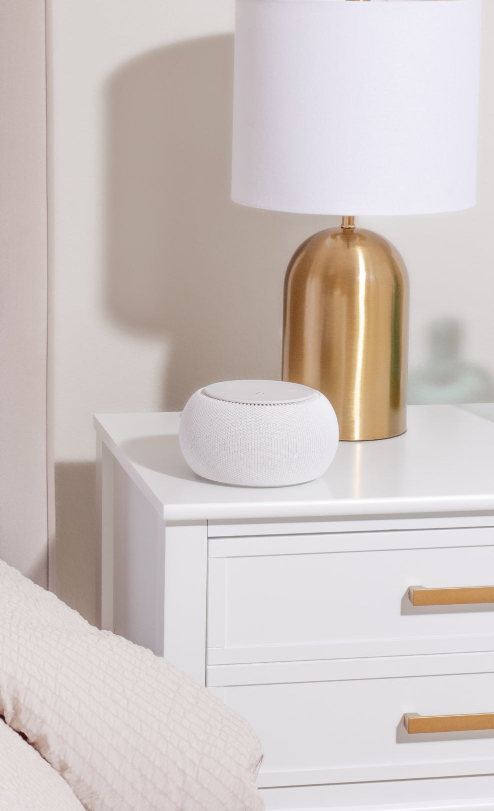 White smart speaker and gold lamp on a white nightstand.
