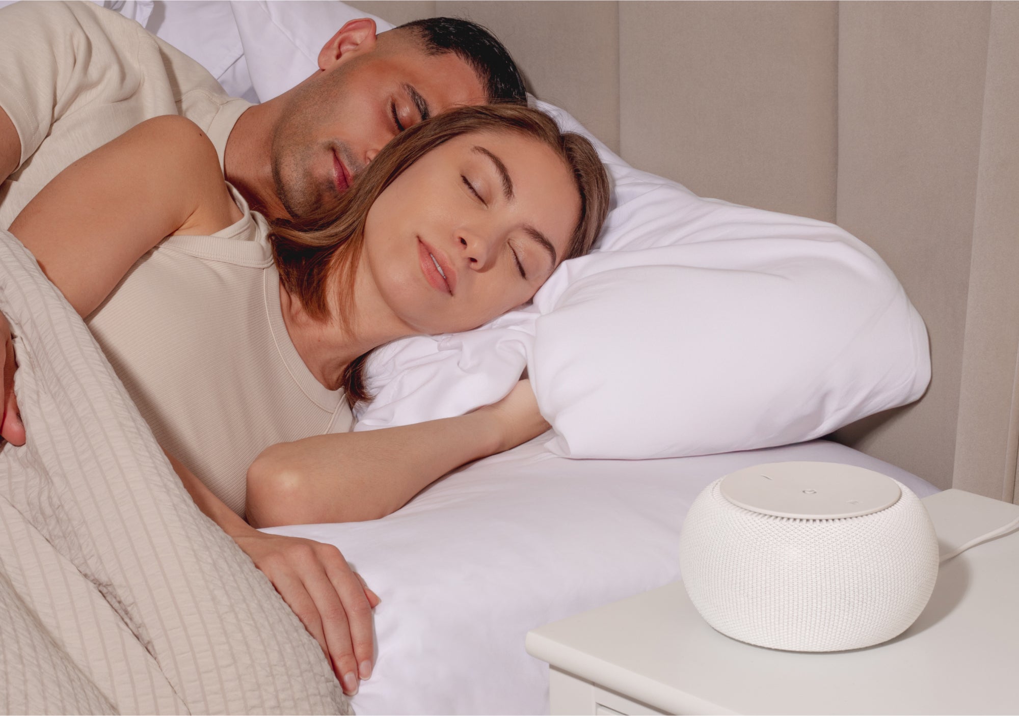 Couple sleeping peacefully with a white smart speaker on the bedside table.